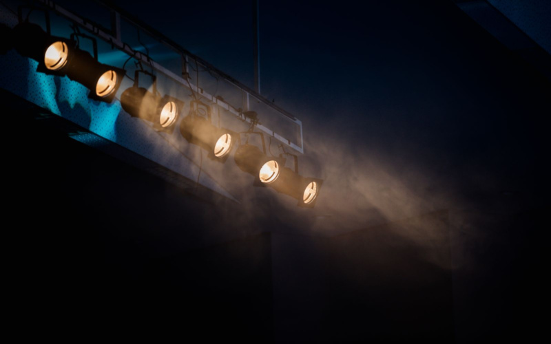 Row of stage spotlights hanging from a ceiling, representing mainstream celebrities crossing into the creator economy