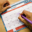 Hands writing on a paper calendar, representing content planning for creators
